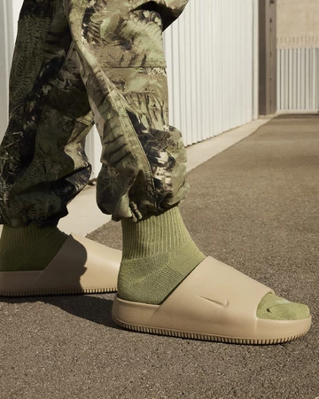 Ein Model trägt die Nike Calm Slide Khaki am Fuß