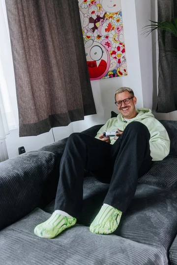 Christopher sitzt auf der Couch und spielt Playstation, dabei trägt er den Palace x Crocs