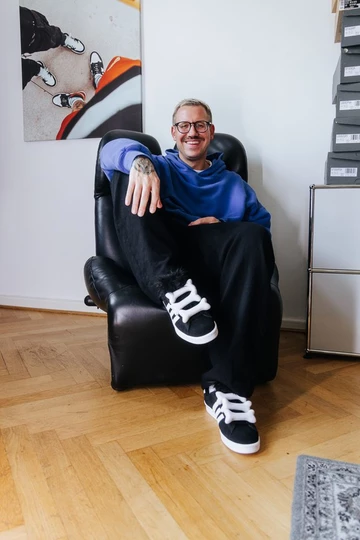 Christopher trägt den Jeremy Scott adidas Campus und sitzt auf einem Sessel