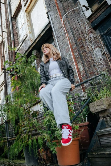 Clara sitzt auf einem Geländer und trägt den adidas Campus 00s Scarlet Red