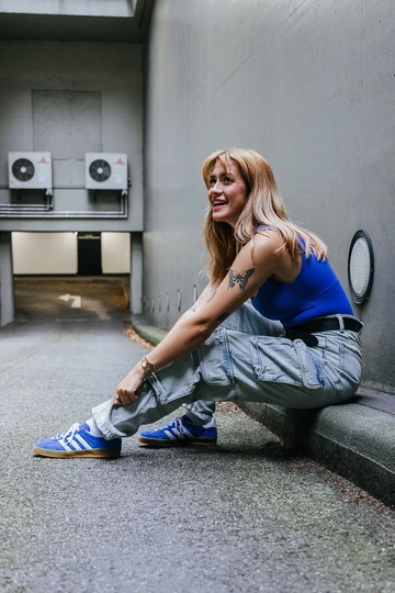 Clara sitzt auf dem Bordstein und trägt die adidas Gazelle Indoor Blue