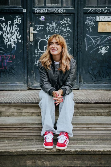 Clara sitzt auf einer Treppe und trägt den adidas Campus 00s Scarlet Red