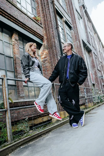 Clara und Christopher stehen an einer Backsteinwand und tragen den adidas Campus 00s