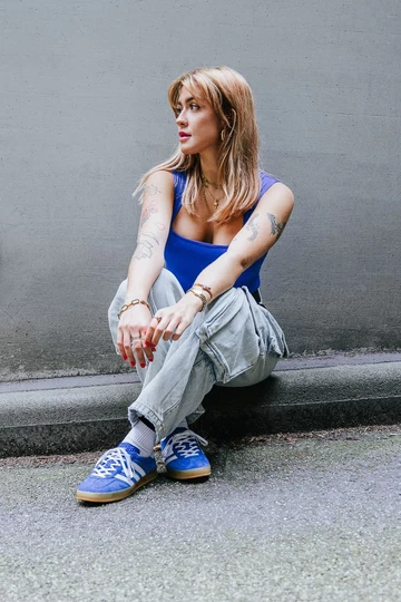 Clara sitzt auf dem Bordstein und trägt die adidas Gazelle Indoor Blue