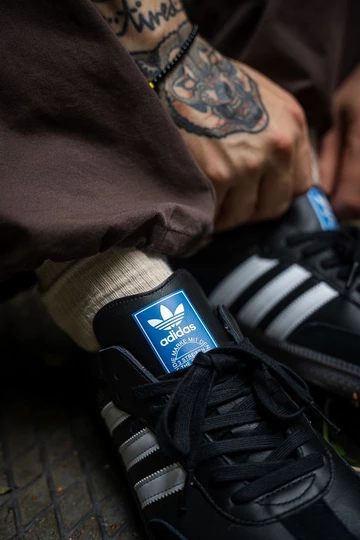 Christopher trägt einen schwarzen adidas Samba in Schwarz mit weißen Streifen.