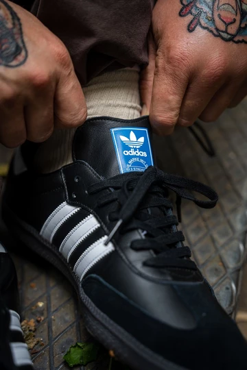 Christopher trägt einen schwarzen adidas Samba in Schwarz mit weißen Streifen.