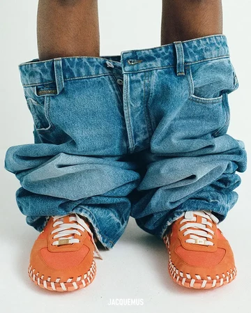 Das Model steht, die Hose ist runtergelassen, man sieht darunter den Jacquemus Air Force 1 Low Bright Mandarin