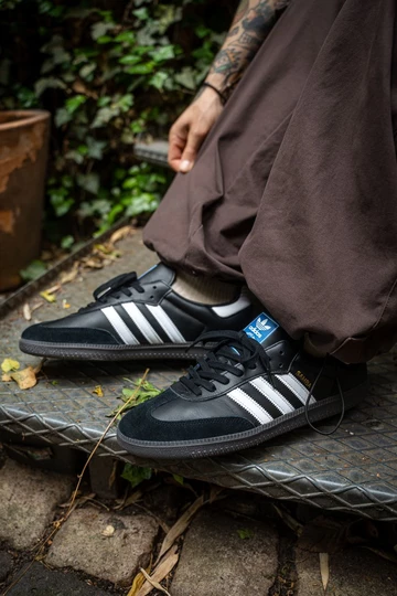 Christopher trägt einen schwarzen adidas Samba in Schwarz mit weißen Streifen.
