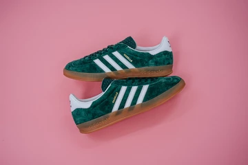Die adidas Gazelle Indoor Green liegt auf rosafarbenem Rollhintergrund