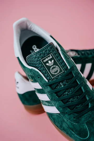 Die adidas Gazelle Indoor Green auf rosafarbenem Rollhintergrund