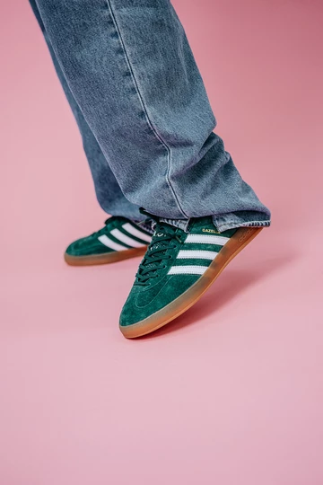 Christopher steht auf einem rosafarbenem Rollhintergrund und trägt die adidas Gazelle Indoor Green