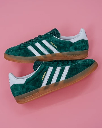 Die adidas Gazelle Indoor Green liegt auf rosafarbenem Rollhintergrund
