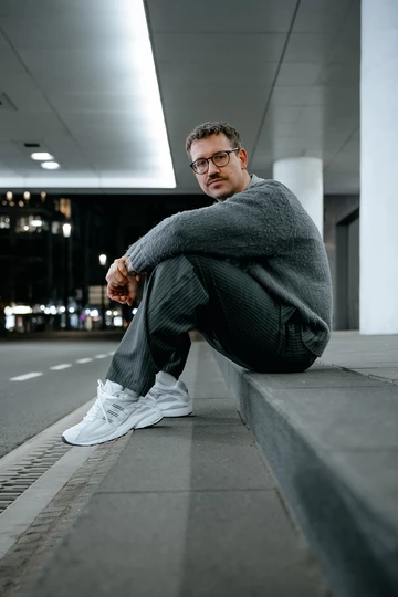 Christopher sitzt auf einem Bordstein und trägt den adidas Adistar Cushion 3 Cloud White am Fuß