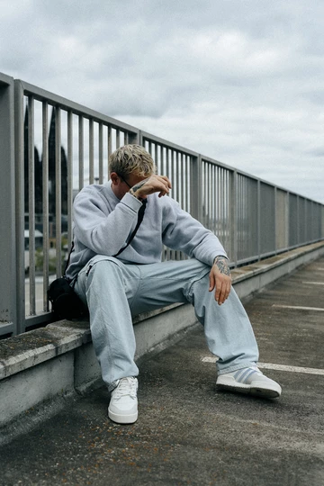 Christopher sitzt auf einer Brüstung, im Hintergrund ist der Kölner Dom und er trägt den BSTN x Real Madrid x adidas Rivalry Low 86