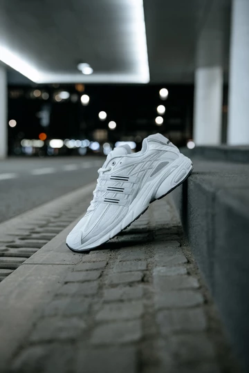 Der adidas Adistar Cushion 3 Cloud White lehnt am Bordstein