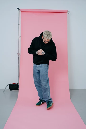 Christopher steht auf einem rosafarbenem Rollhintergrund und trägt die adidas Gazelle Indoor Green