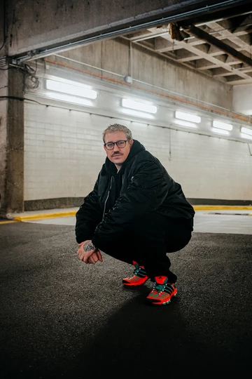 Christopher hockt in einem Parkhaus und trägt den adidas adistar Raven im Colorway Solar Orange