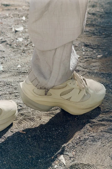 Der AURALEE New Balance WRPD Runner in Bone am Fuß eines Models