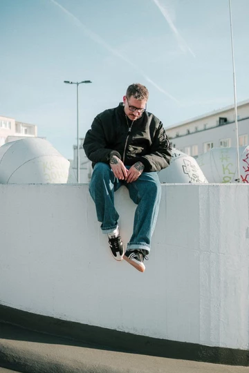Christopher sitzt auf einer Mauer und trägt den adidas Samba Black Wonder White im Wales Bonner Style