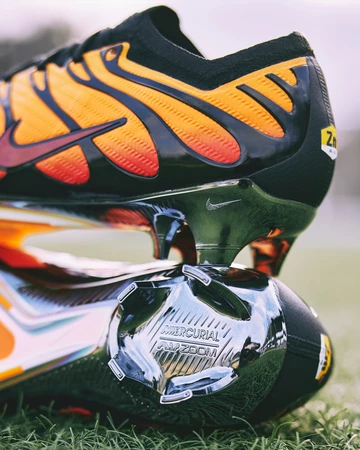 Der Air Max Plus Mercurial Vapor 15 Pimento liegt auf einem Fußballplatz