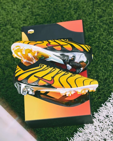 Der Air Max Plus Mercurial Vapor 15 Pimento liegt auf einem Fußballplatz auf seinem Karton