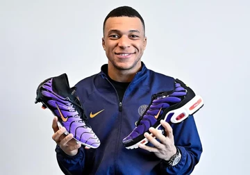 Kylian Mbappé hält den Nike Mercurial Superfly 9 FG Voltage Purple und den OG Air Max Plus in der Hand
